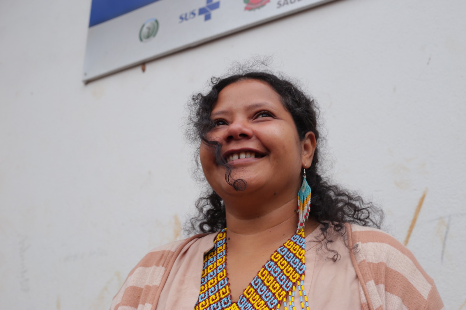 A foto mostra a personagem Poty Poran, uma mulher indígena com cabelos enrolados, sorrindo. Ela usa ainda colar e brincos de miçangas nas cores azul e amarelo